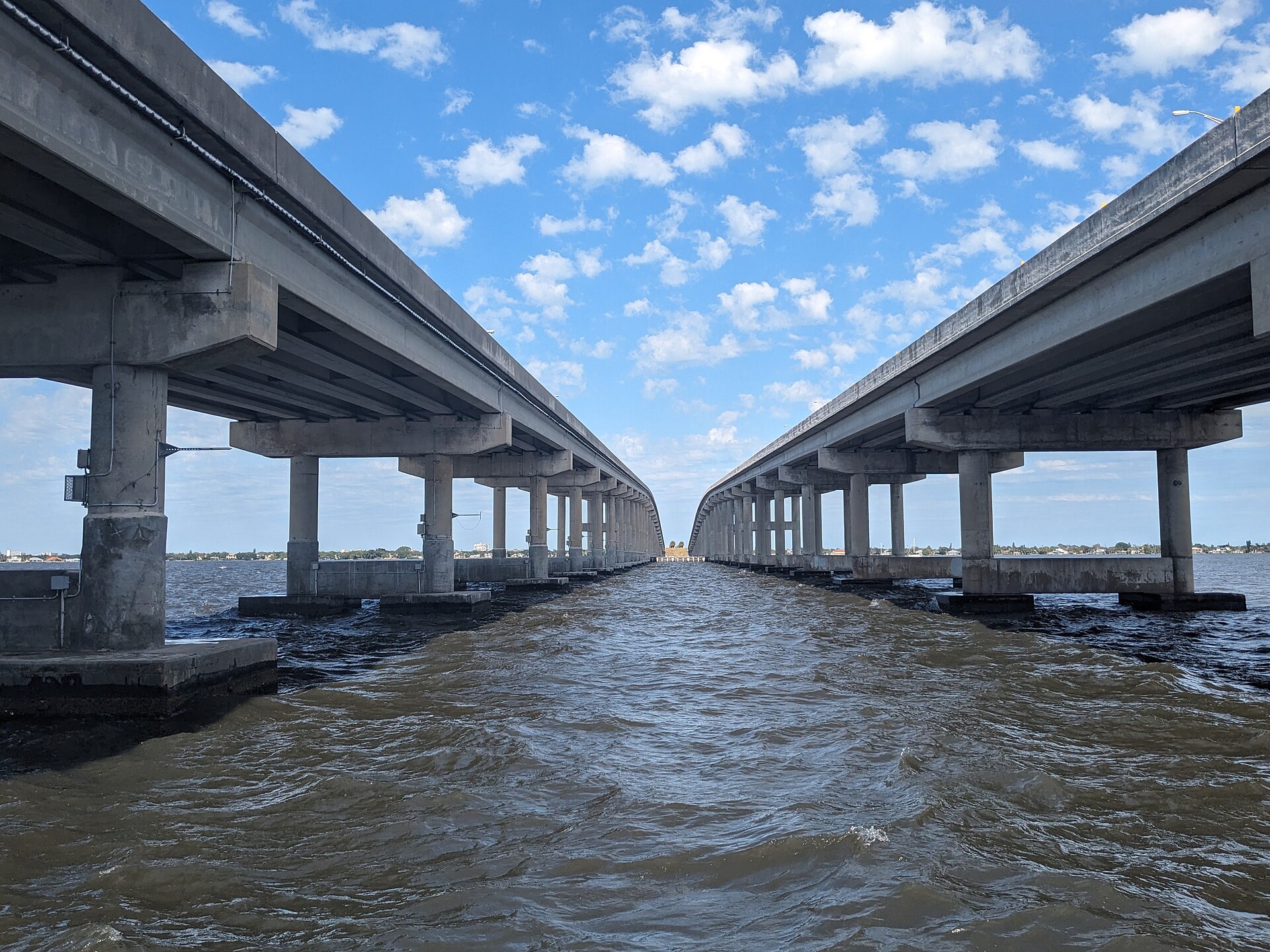 A view of the two spans of the Melbourne Causeway crossing the Indian River Lagoon, with calm water and palm-lined banks visible.